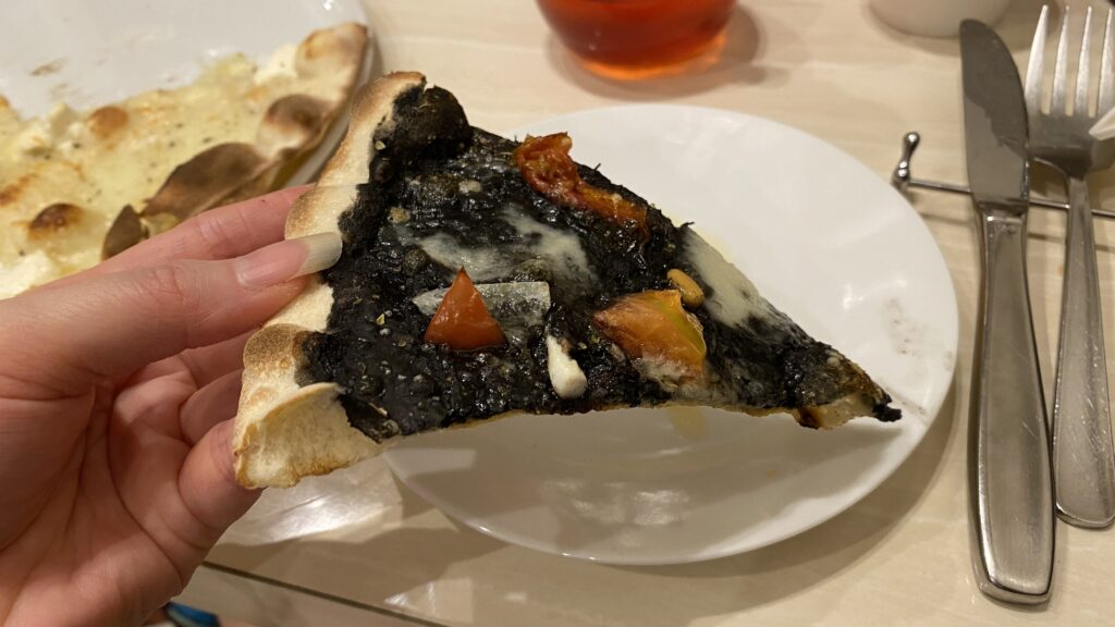 holding a slice of Squid Ink Sauce Pizza in hand